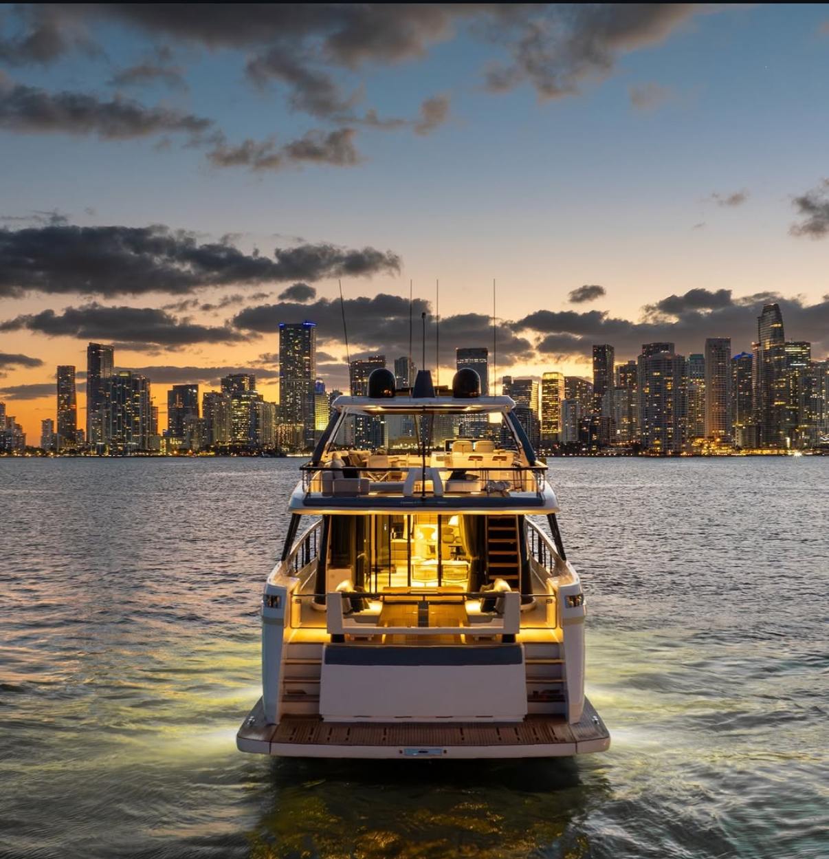 A delivered yacht seen from astern at dusk, with the Miami skyline behind it. M2Develop