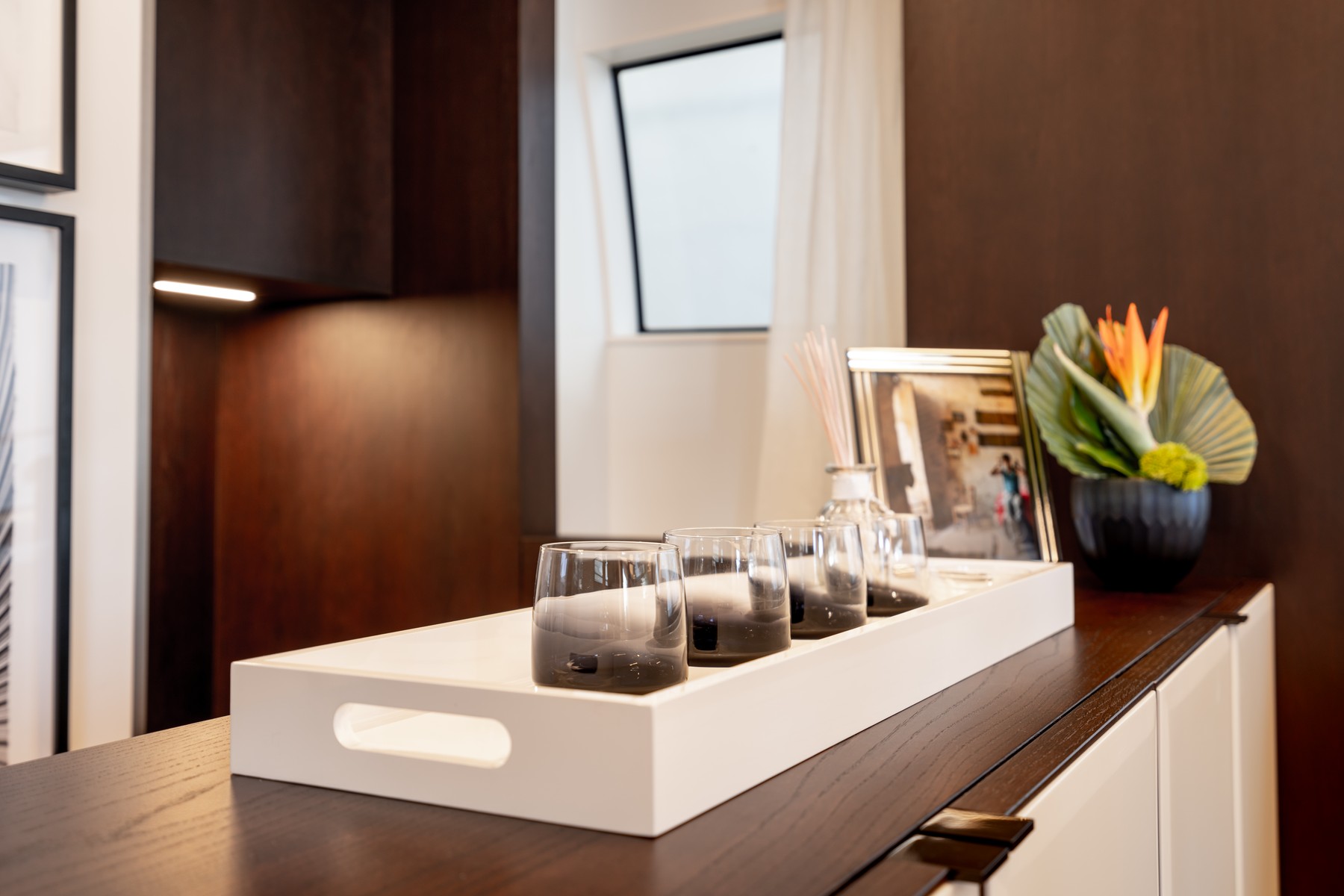 A tray of glasses, framed photographs and a plant arranged on a credenza in a yacht salon.