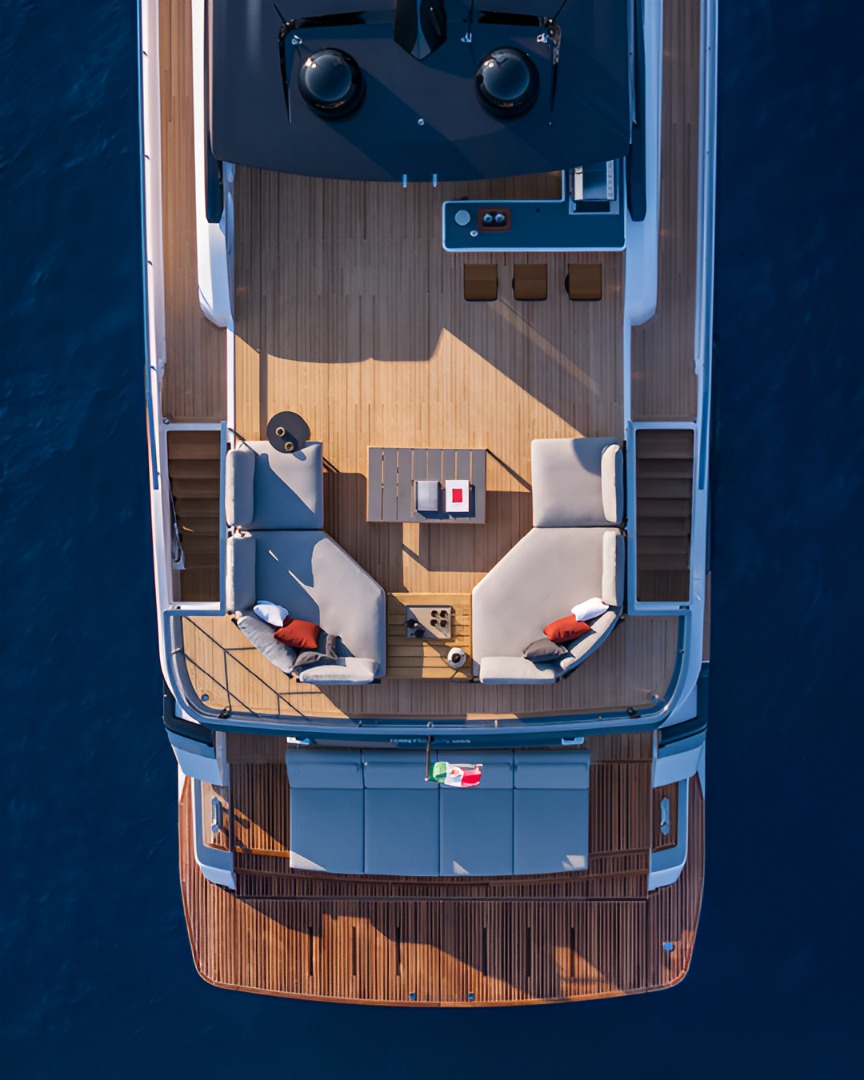 A delivered yacht's aft deck from overhead, twin sofas on the teak and deep blue water alongside.